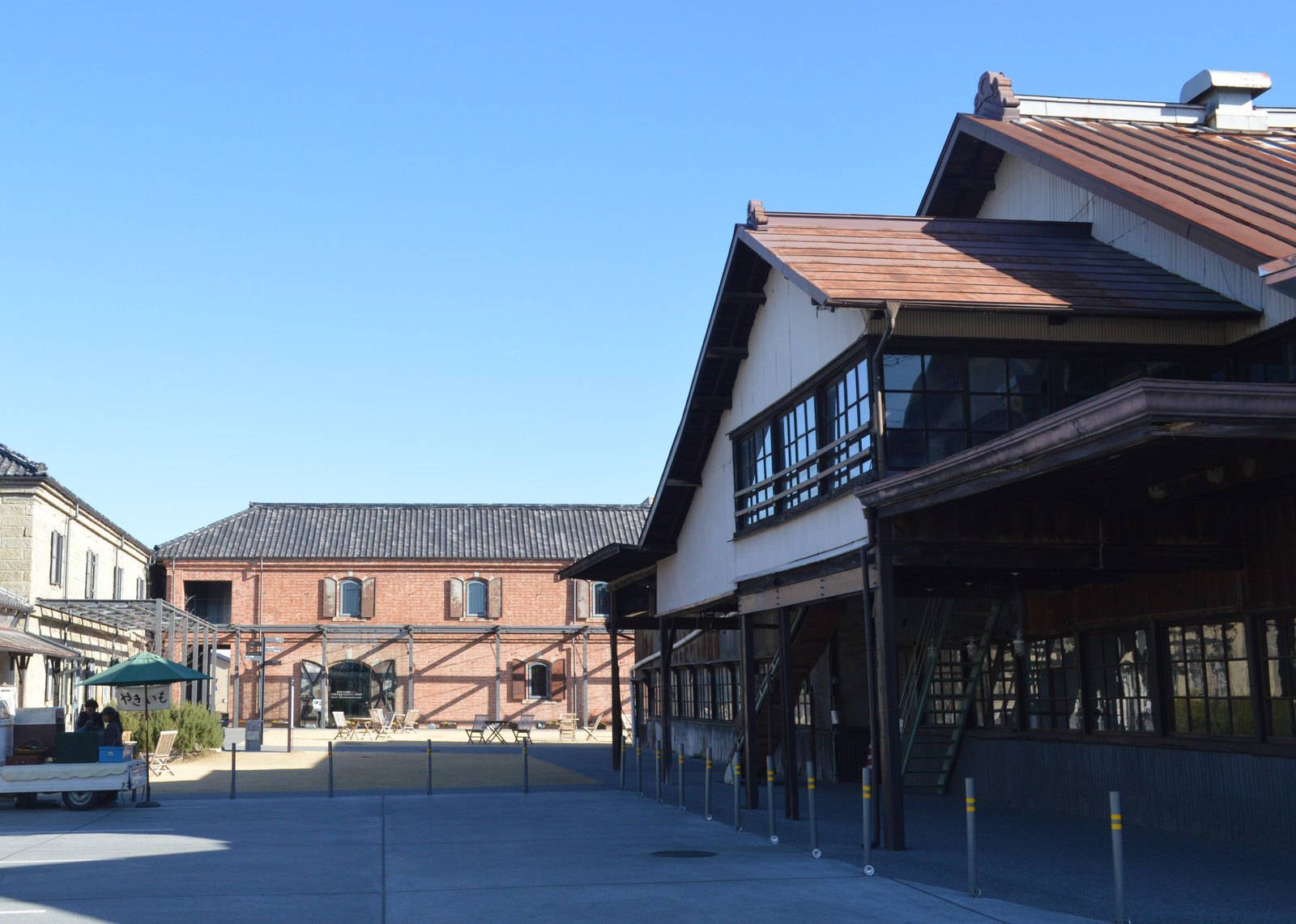 旧富岡倉庫の広場。正面奥に瓦屋根の煉瓦積みの倉庫、右手前に木造の大きな建物、左端に石積みの倉庫の一部が見える