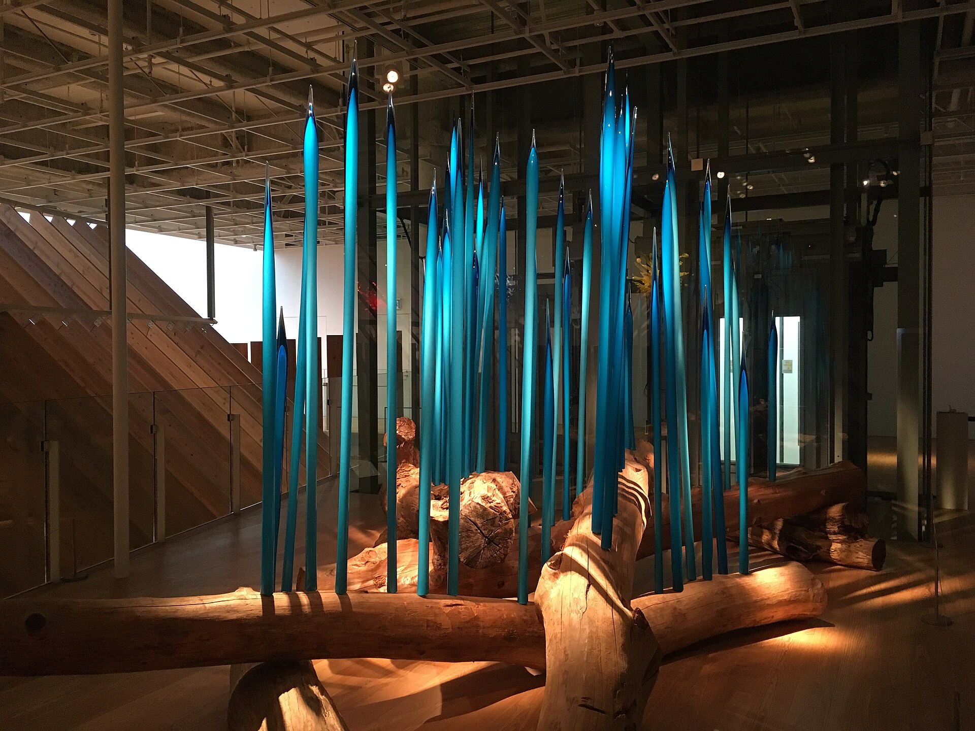 木の丸太の間に、青いガラスの細長い造形が林立する、富山市ガラス美術館の館内展示