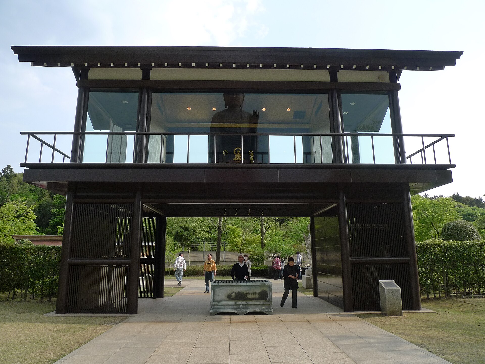 森を背にした、ガラス張りの二階建ての門のような建物と、手前の大香炉