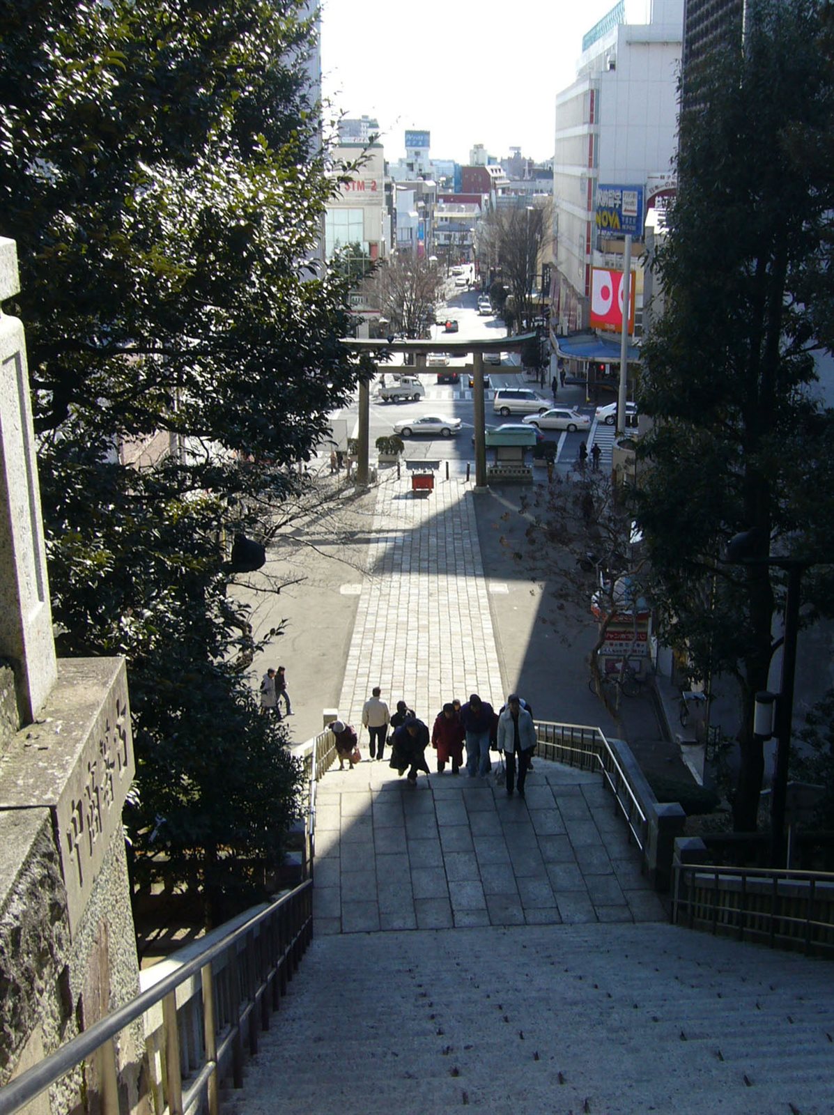 宇都宮二荒山神社の石段を上から見下ろした写真。幅の広い石段の下に鳥居があり、その先に市街地の大通りとビルが続いている。石段を数人が上ってくる