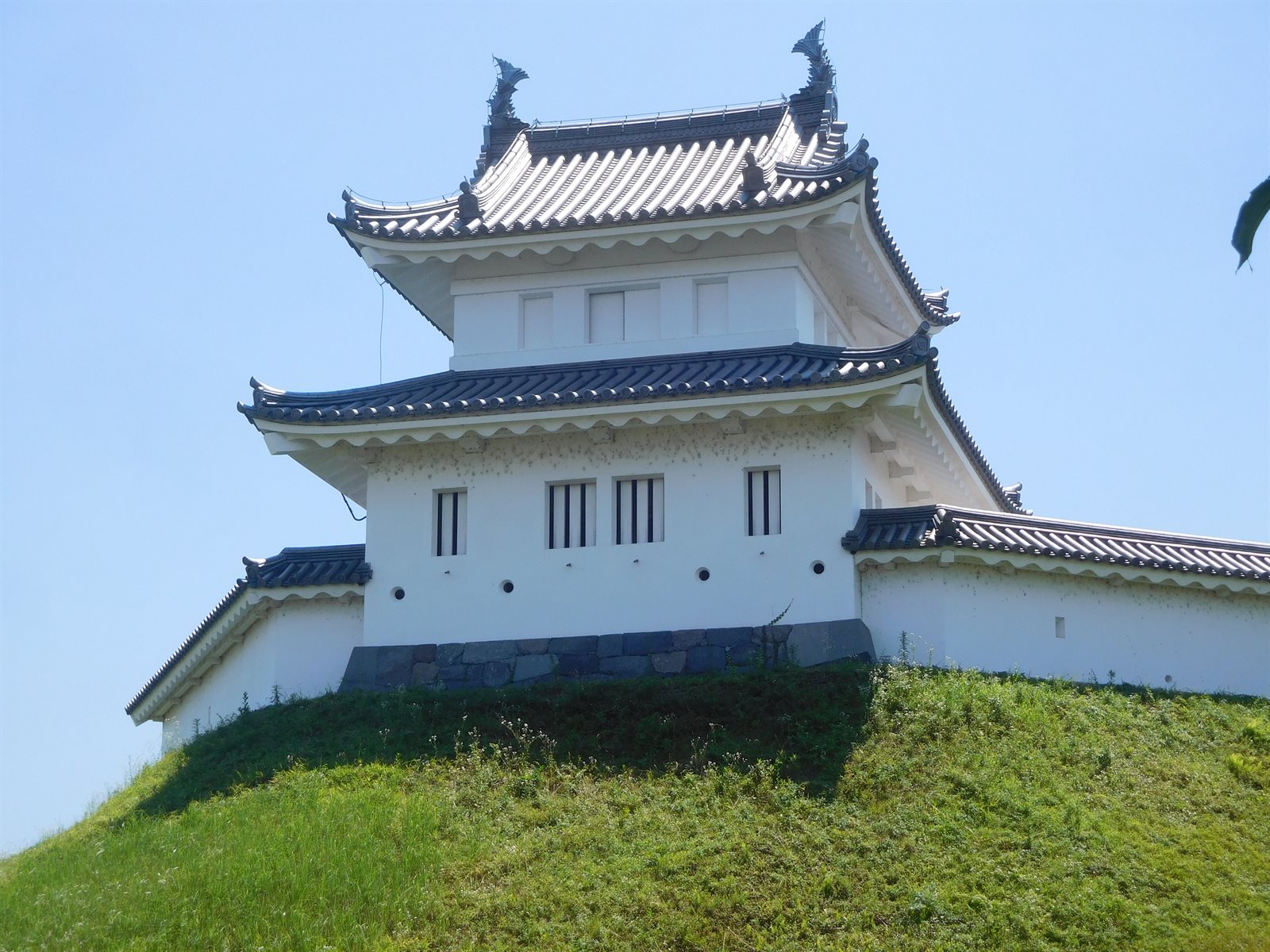 宇都宮城址公園の清明台。草に覆われた土塁の上に、白い漆喰壁と瓦屋根の二重の櫓が建ち、左右に白い塀が続いている