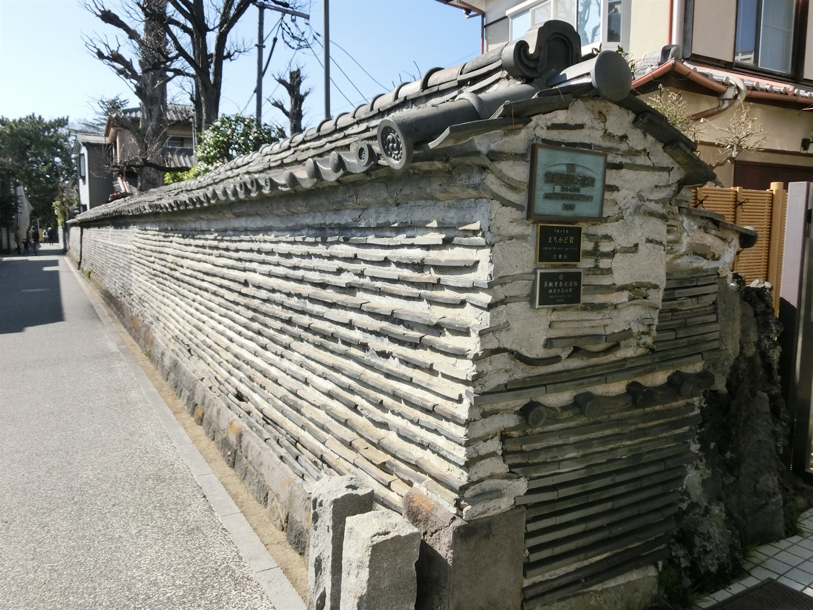 観音寺の築地塀。瓦と土を交互に積み上げた塀が道沿いに長く続き、上に瓦屋根がかかっている。塀の端に説明板が取り付けられている