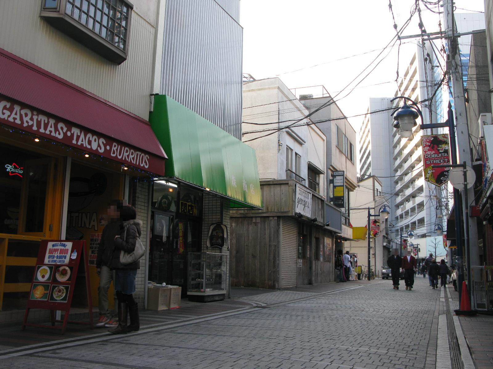 どぶ板通りの石畳の通り。英語の看板を掲げた飲食店や商店が並び、街灯に「DOBUITA STREET」の旗が下がっている