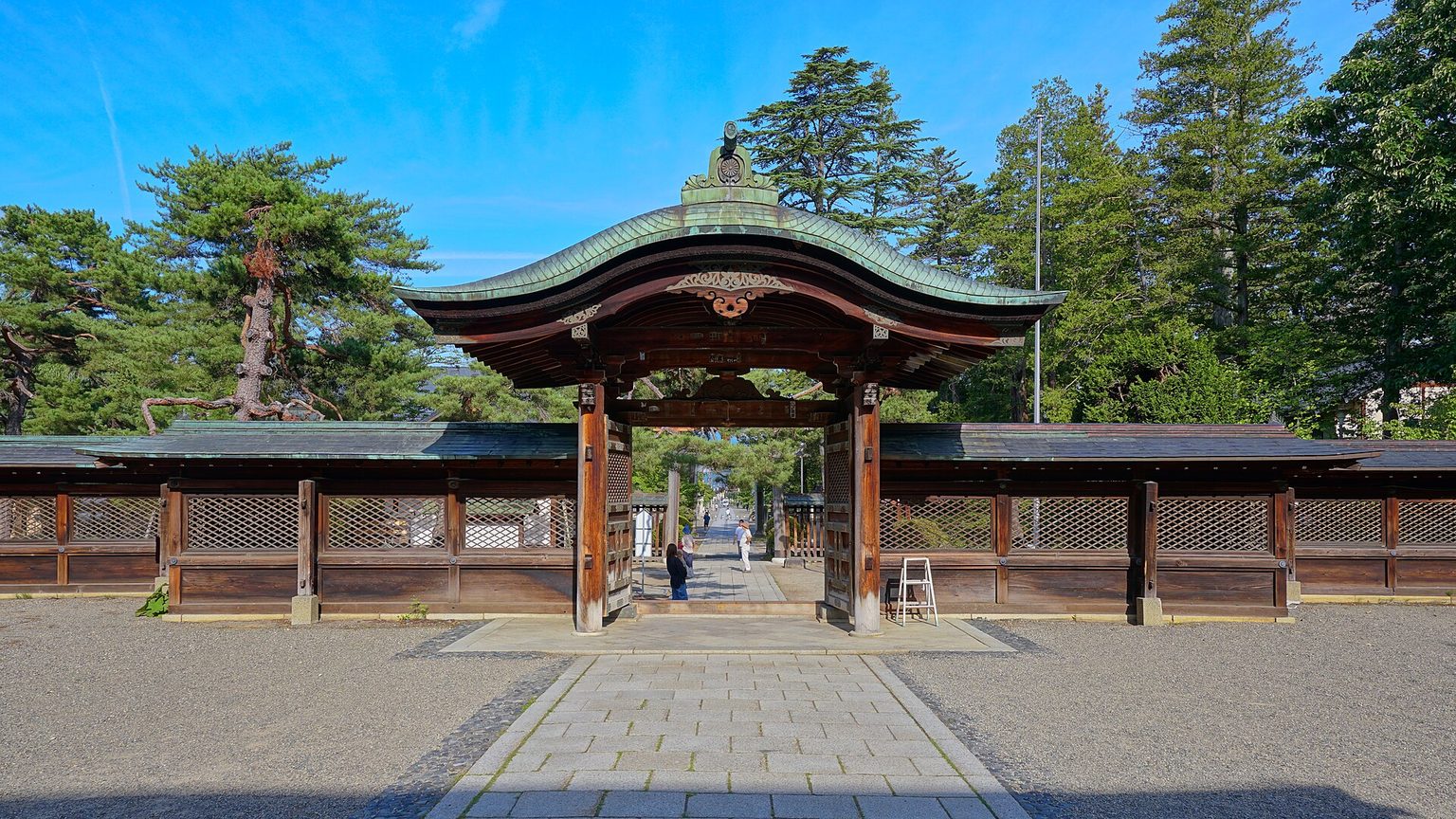 朱色と緑青の屋根を持つ唐門が、石畳の参道の先に建つ上杉神社