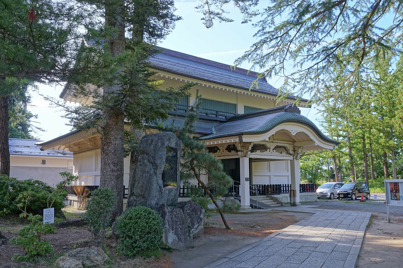 松の木の間に建つ、瓦屋根の稽照殿と、入口の前の庭石