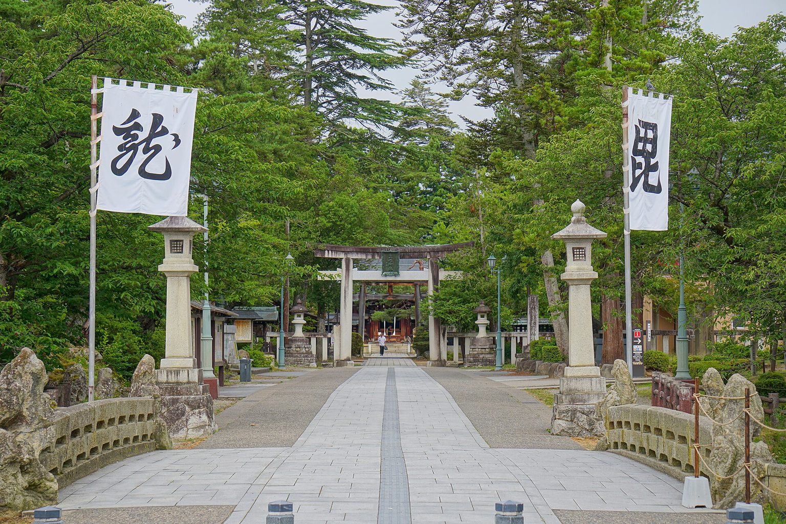 幟が立つ石畳の参道の先に鳥居が見える、緑に囲まれた上杉神社
