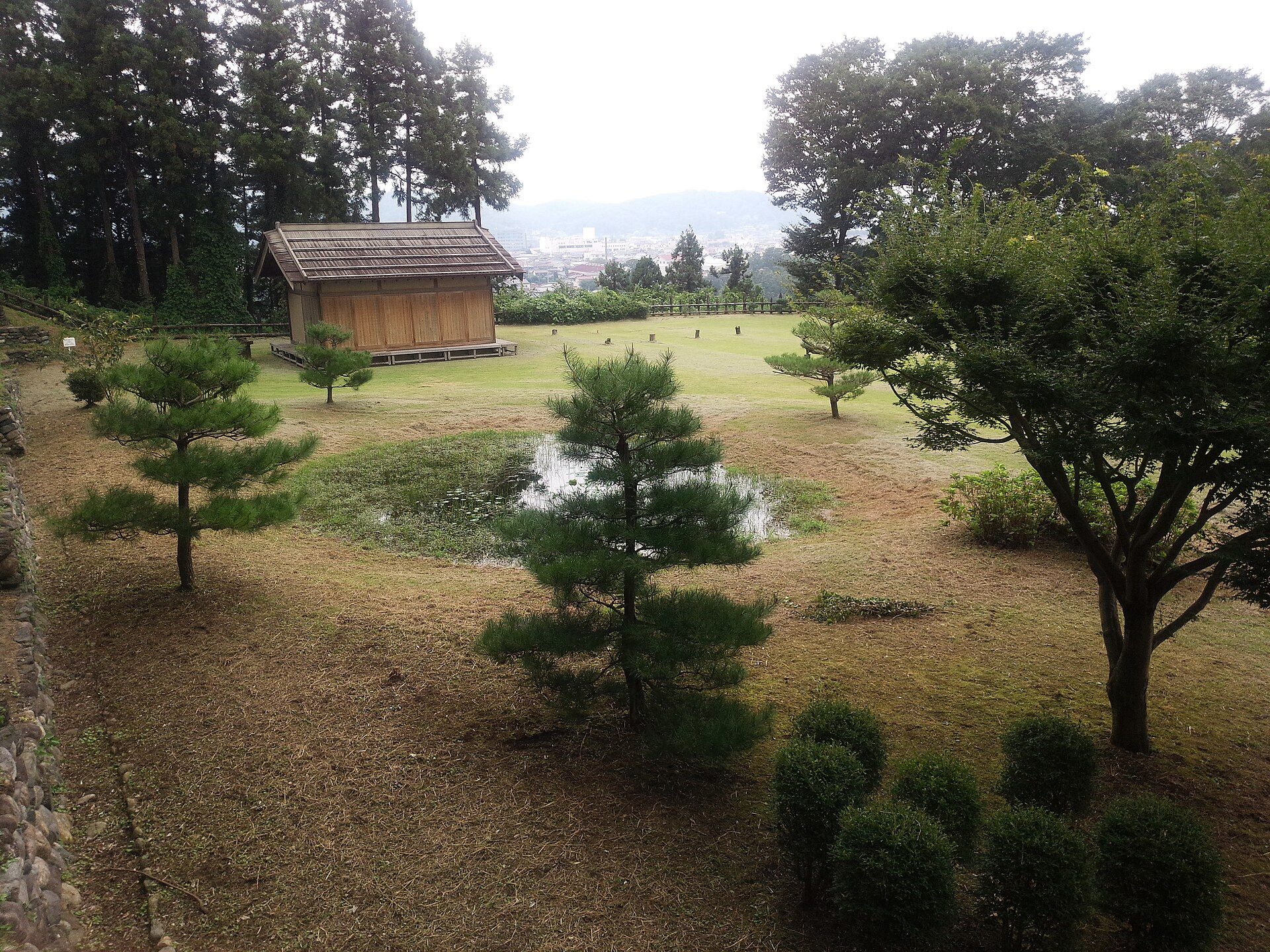 石積みの土塁の内側に、復元された小屋と池が広がる鉢形城跡