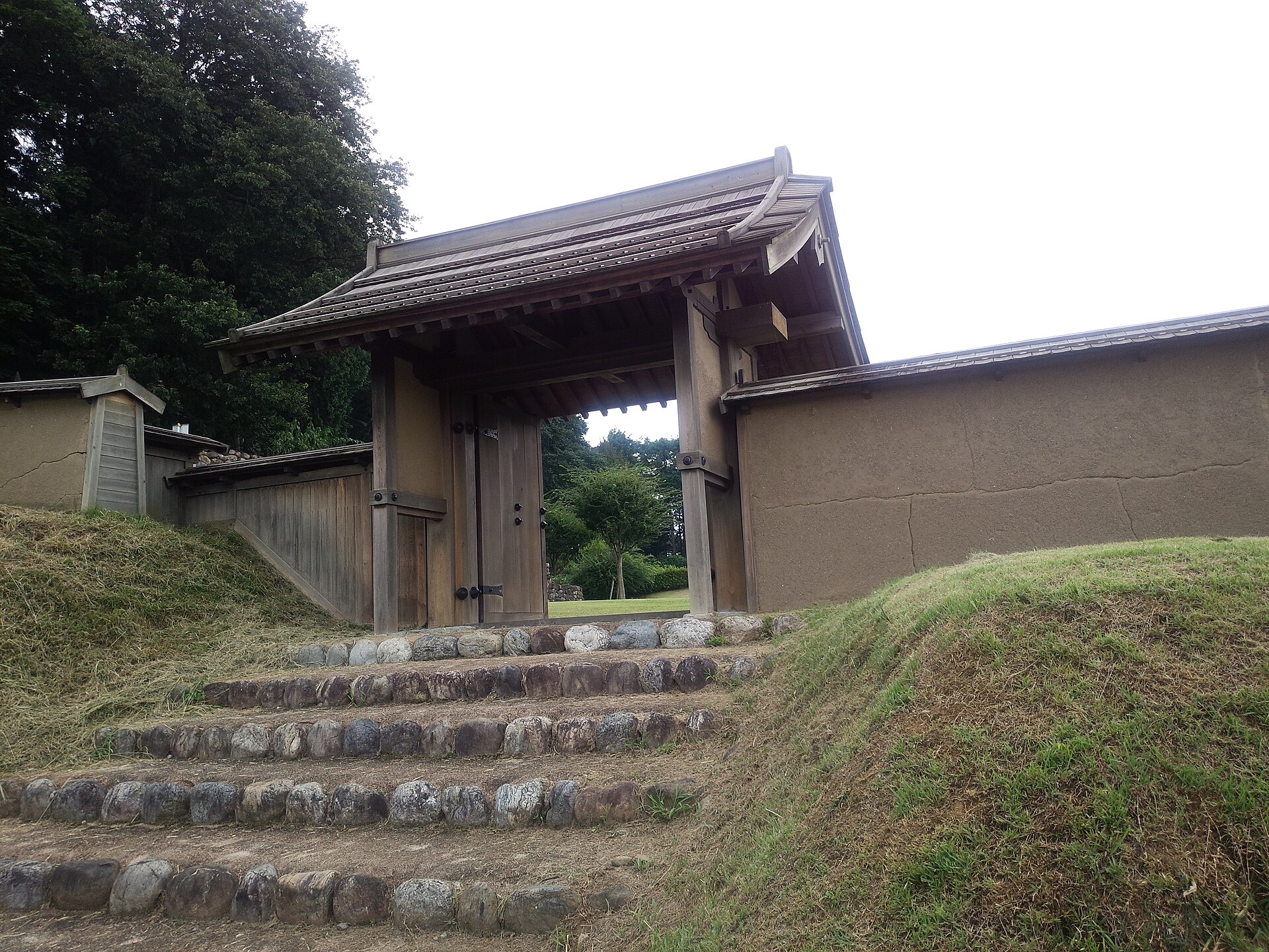 土塁の間に立つ、復元された鉢形城の木造の門と石を並べた階段