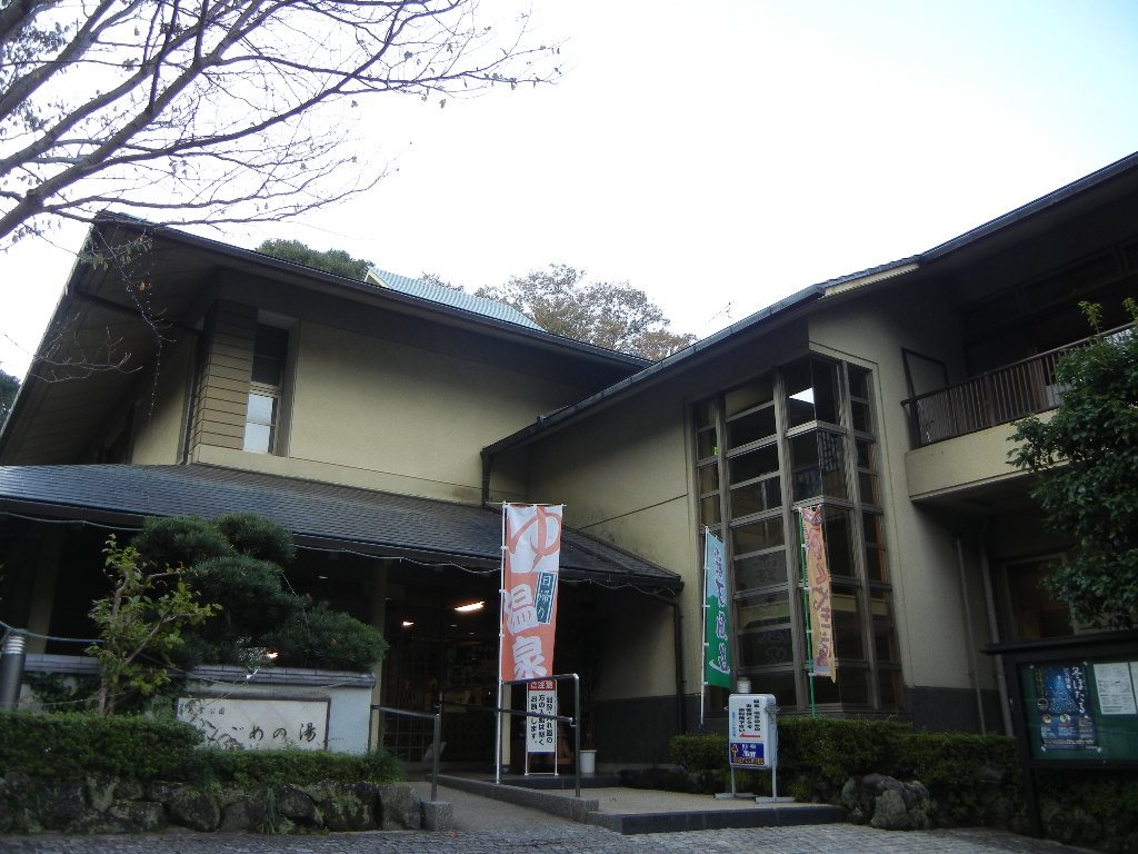 こごめの湯の外観。瓦屋根の二階建ての建物の前に「日帰り温泉」ののぼりが立ち、左手の白壁に施設名が刻まれている