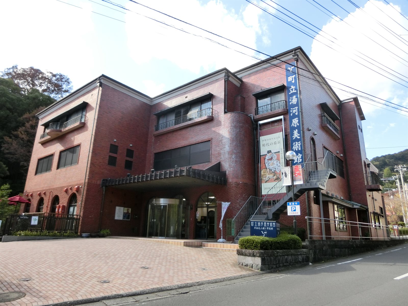 町立湯河原美術館の外観。赤レンガの建物の右手に館名を縦書きにした看板が掲げられ、手前に石畳の前庭が広がっている