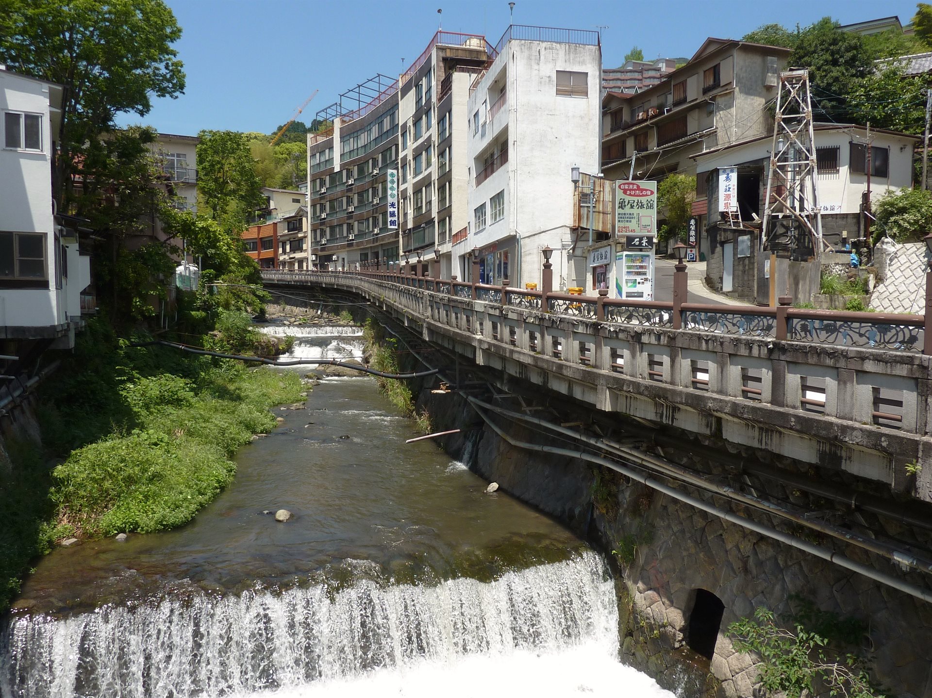 湯河原温泉の藤木川。川沿いの道に旅館や商店が並び、手前で水が堰を越えて白く落ちている