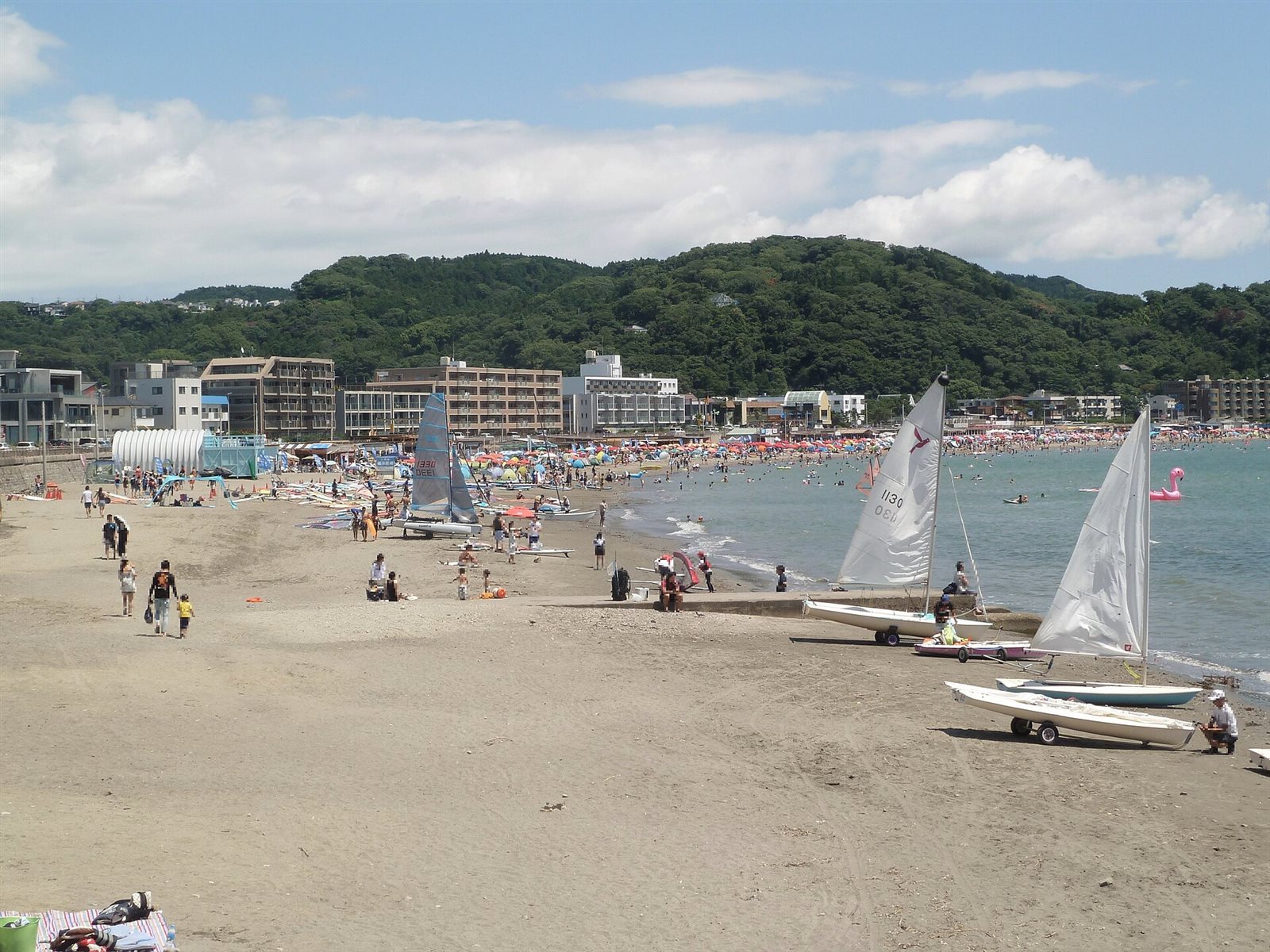砂浜にヨットが並び、奥に緑の山が続く、夏の逗子海岸
